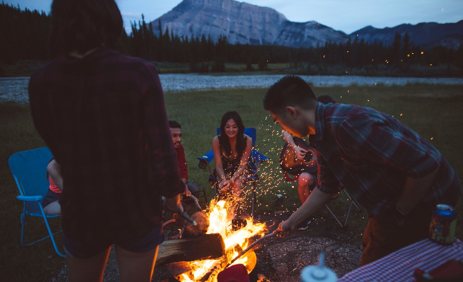 Friends sit around the campfire at Cascade Ponds with Mount Rundle in the background in Banff National Park.